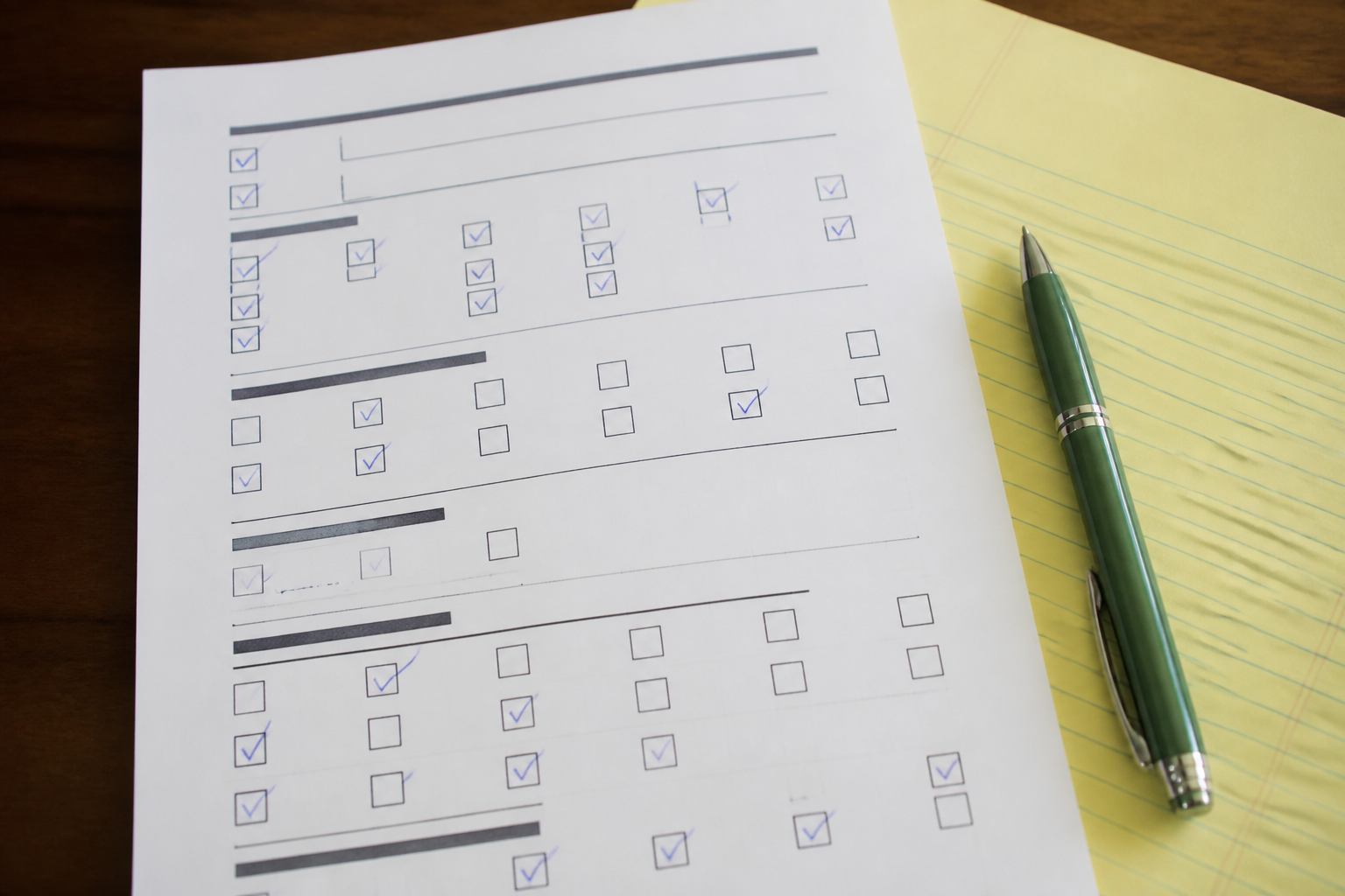 A printed checkbox form and a green pen on blotter paper.